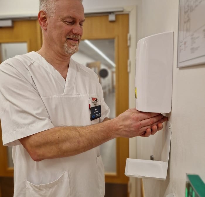 Ansatt tar antibac på hendene fra dispenser på veggen.